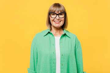 Elderly smiling happy cheerful fun satisfied blonde woman 50s years old wear green shirt glasses casual clothes looking camera isolated on plain yellow background studio portrait. Lifestyle concept.
