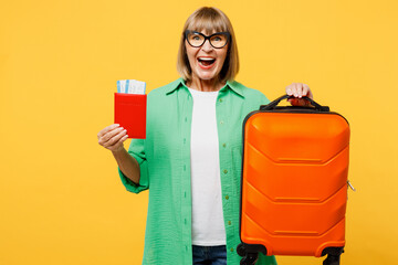 Traveler happy elderly woman wear casual clothes hold passport ticket bag isolated on plain yellow background. Tourist travel abroad in free spare time rest getaway. Air flight trip journey concept.