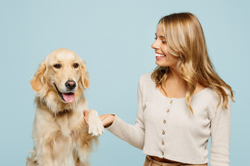 Young happy owner woman casual clothes teaching new commands her best friend retriever dog wear, hold paw isolated on plain pastel light blue background studio. Take care about pet, contact concept.