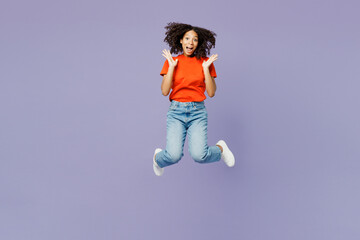 Full body happy little kid teen girl of African American ethnicity wear orange t-shirt jump high spread hands look camera isolated on plain pastel purple background studio Childhood lifestyle concept