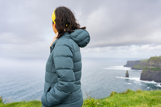 Unrecognizable woman from behind with backpack contemplating a beautiful seascape from the top of the cliffs in Ireland