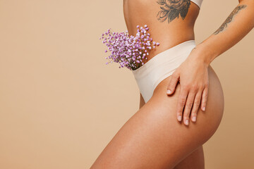 Close up cropped side view young nice lady woman with slim body perfect skin wears nude top bra lingerie stand with flowers in panties isolated on plain beige background. Lifestyle diet fit concept. - obrazy, fototapety, plakaty