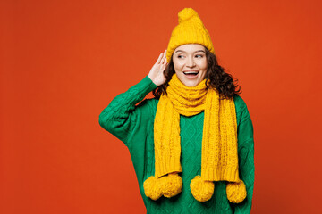 Young smiling happy curious woman she wear green knitted sweater yellow hat scarf try to hear you...