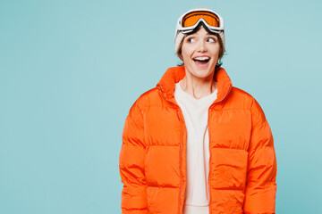 Skier cheerful amazed young woman wears warm padded windbreaker jacket hat ski goggles mask look aside on area travel rest spend weekend winter season in mountains isolated on plain blue background.