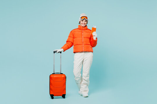 Traveler skier woman she wear padded windbreaker jacket ski goggles mask hold passport ticket bag isolated on plain blue background Tourist travel abroad in free time rest getaway. Air flight concept
