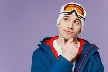 Skier minded man wear warm blue jacket ski goggles mask put hand prop up on chin, lost in thought look aside spend weekend winter season in mountains isolated on plain purple background Hobby concept