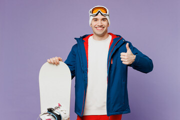 Smiling man wears warm blue windbreaker jacket ski goggles mask hat hold snowboard showing thumb up...