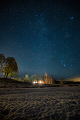 Milky Way stars in the blue sky directly above the red Swedish wooden house and trees in the garden...