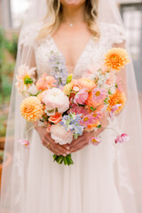 A close-up of a bride holding a soft wedding bouquet in pastels and soft pinks. 