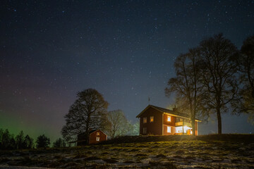 Winter landscape with wooden house under a beautiful starry sky and Northern Lights - obrazy, fototapety, plakaty