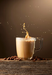 Glass cup of coffee drink, latte or mocha with splashes on a brown background.