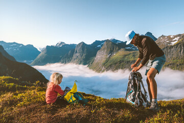 Family travel father and daughter packing backpacks vacations in mountains dad with child hiking together active adventure trip camping gear outdoor parent and kid girl climbing in Norway above clouds - 697360123
