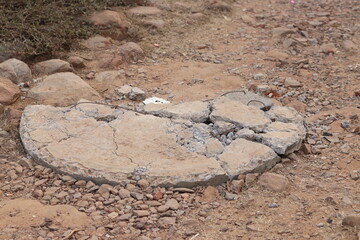 Old broken sewer hole cap made up of cement in a dirt ground, closeup