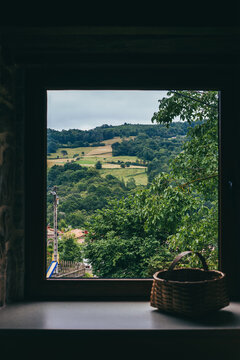 Fototapeta Front view of natural landscape as seen from the window of a house with a wicker basket on the window sill. Concept of nature and rural lifestyle