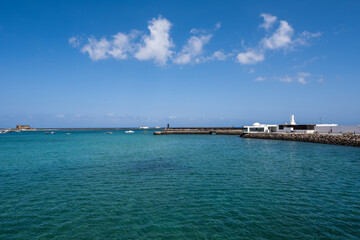Fototapeta na wymiar View of the Fermina islet. Turquoise blue water. Sky with big white clouds. Seascape. Lanzarote, Canary Islands, Spain.