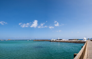 Fototapeta premium View of the Fermina islet and wooden access bridge. Turquoise blue water. Sky with big white clouds. Seascape. Lanzarote, Canary Islands, Spain.