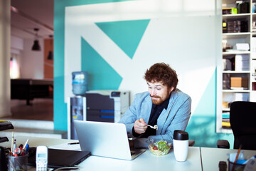 Young man eating salad while working in office