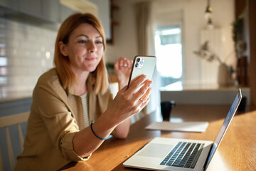 Young woman using smartphone with her laptop open in front of her