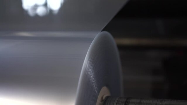 Automatic polyethylene plastic bag production machine with lighting effect. Close-up of the roller of the plastic bag production machine in the light blue scene. Chemical production of the bopp film
