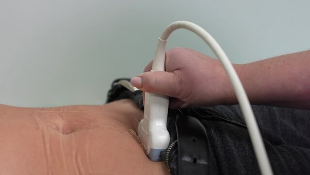 Ultrasound diagnosis of the stomach on the abdominal cavity of a man in the clinic, close-up view. The doctor runs an ultrasound sensor over the patient's male abdomen. Diagnostics of internal 

