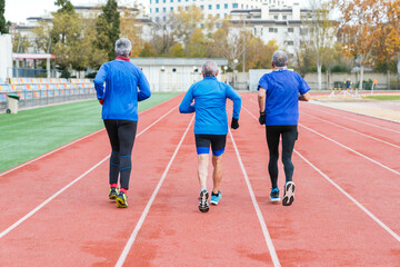 Three senior male runners in blue sportswear train on an athletic track, showcasing active lifestyle and teamwork in sports.