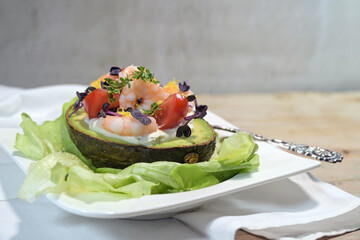 Filled avocado with shrimps, tomatoes, mayonnaise and cress garnish on lettuce and a white plate,...