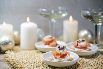 Festive canapes with shrimps and salmon, champagne drink glasses and candles, appetizer snack for a holiday party on Christmas or New Year, copy space, selected focus - obrazy, fototapety, plakaty