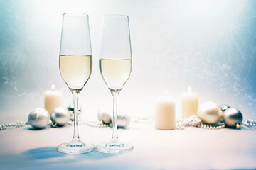Two champagne flute glasses, candles and festive Christmas decoration against a blue gray background with light party bokeh for a happy New Year, copy space, selected focus