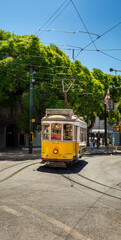 Fototapeta premium Famous and typical old yellow tram, beautifully decorated and preserving the original designs traveling uphill on the tracks of a typical Lisbon street in Portugal.