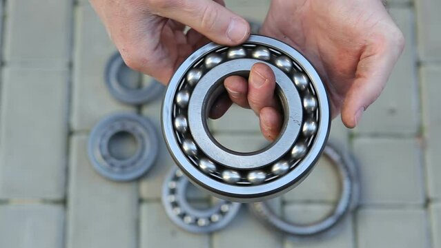 A man holds and rotates a large rolling bearing in his hands, against the background of different bearings.