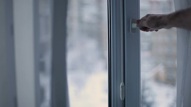 A man opens a window in an apartment for ventilation on a frosty winter day.
