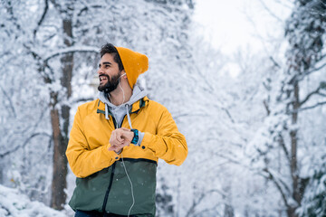 Confident handsome man with beanie and beard tracking fitness progress on smart watch and listening...