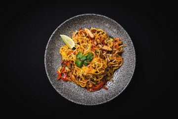 Appetizing pasta with herbs, vegetables and seafood on a black background.