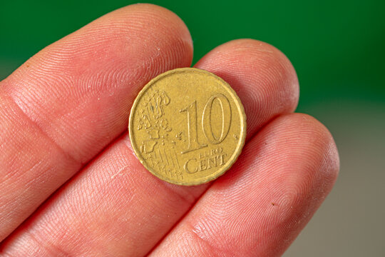 coin face of 10 euro cents in the fingers of the hand. green background.
