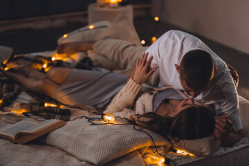 Beautiful happy loving young smiling couple relaxing in bed, watching movies on projector. Cozy home atmosphere, tenderness, closeness. Romantic surprise, atmospheric candles, Saint Valentine's Day - Powered by Adobe