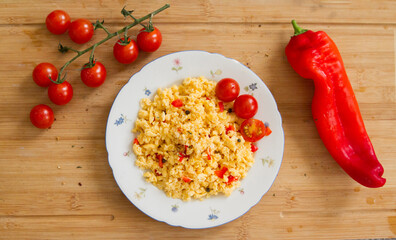 Leckeres Frühstück, Rührei mit Tomaten und Paprika auf einem weißen Blumenteller auf einem rustikalen Holztisch
