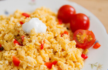 Leckeres Frühstück, Rührei mit Tomaten und Paprika auf einem weißen Blumenteller auf einem rustikalen Holztisch