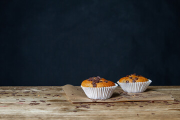Frisch gebackene Schokoladenmuffins auf Geschirrtuch mit rustikalem Tisch und schwarzem Hintergrund