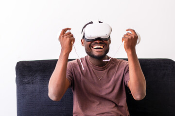 young man wearing a vr headset engrossed in a virtual reality game and holding controllers sitting...