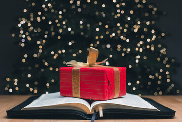 The open book of the Holy Bible. Gift. On the background is a Christmas tree. Christmas and New...