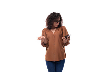 a young slender woman with a curly haircut is dressed in a brown shirt holding a phone in her hand