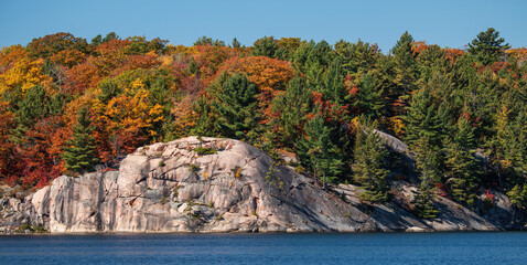 large rock face on shoreline with fall colours George Lake Killarney Pro. park Ontario Canada