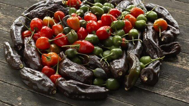 Heap of ripe and unripe Brazilian Red Olive and Peruvian Machu Picchu chilies on a wooden table. Table spin.