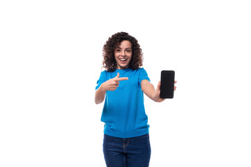 young woman with curls dressed in a blue t-shirt shows the screen of a mobile phone with a mockup
