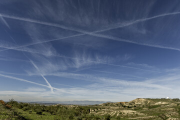 A skyscape with several traces of aviation fuel and some small mountains with a radar under a...