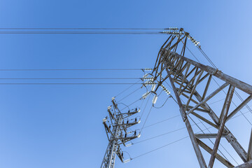 Some high voltage towers with electrical wiring in a low angle image with the sky in the background