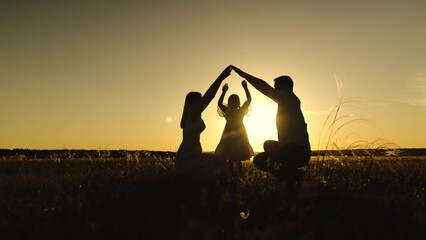 Silhouettes of parents against sky over daughter holding hands with setting sun. Figures of parents...