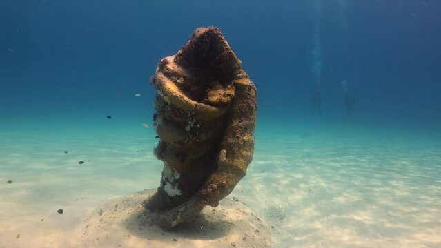 paisaje subacuatico de aguas cristalinas del mar caribe y una estatua con forma de concha y silueta de virgen sumergida en el mar.