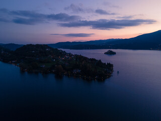 San Giulio Island within Lake Orta in Piedmont, Italy. aerial drone view at sunset blue hour. city lights and colorful sky