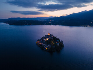 San Giulio Island within Lake Orta in Piedmont, Italy. aerial drone view at sunset blue hour. city...